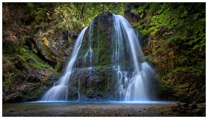Versteckt im Wald bei Schliersee st&uuml;rzt der Josefsthaler Wasserfall in eleganten Schleiern &uuml;ber moosbewachsene Felsen. Das leise Rauschen und das klare Wasser schaffen einen Ort der Ruhe und nat&uuml;rlichen Sch&ouml;nheit im Herzen der bayerischen Alpen.