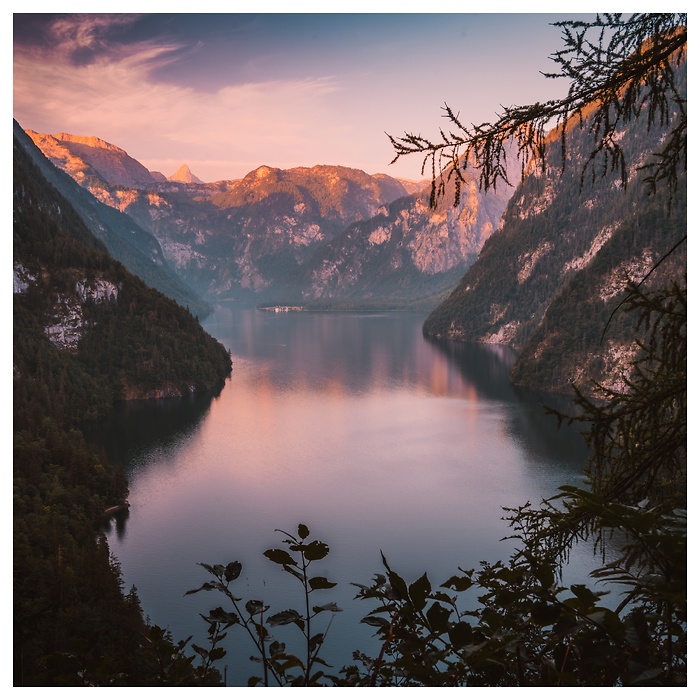 Im ersten Licht des Tages liegt der K&ouml;nigssee ruhig zwischen steilen Alpenw&auml;nden. Zarte Pastellfarben am Himmel spiegeln sich im glatten Wasser und verleihen der Szene eine klare, friedliche Morgenstimmung fernab von Trubel und Zeit.