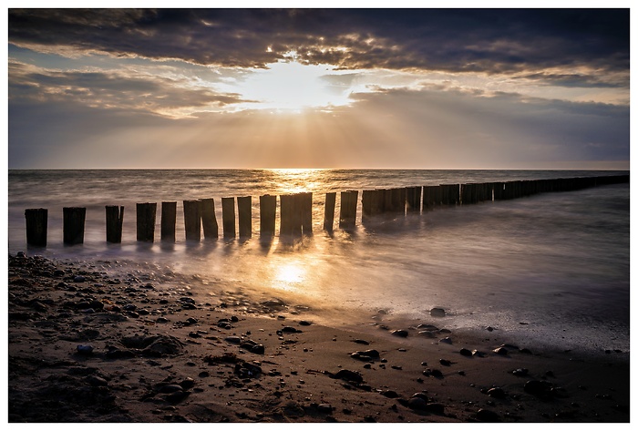 Der Moment, wenn die Sonne sich durch die Wolken bricht und das Meer in flüssiges Gold taucht. Zwischen den Buhnen fließt die Zeit einfach davon. Küstenruhe im Abendlicht.