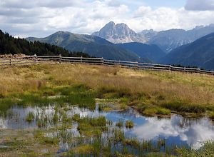 Mountain landscape of the Lüsener Alm with clouds reflected in the water of a small pond.
