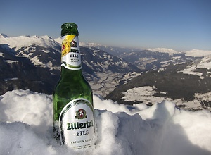 A Zillertal beer bottle stands on the summit in the snow.