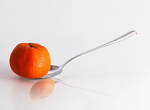 An orange tangerine balanced on a spoon.
